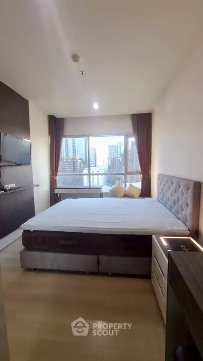 Modern bedroom with city view, featuring a large bed and wall-mounted TV.