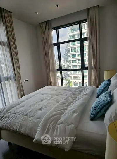 Luxurious bedroom with large window offering stunning city view, elegant decor and plush bedding.