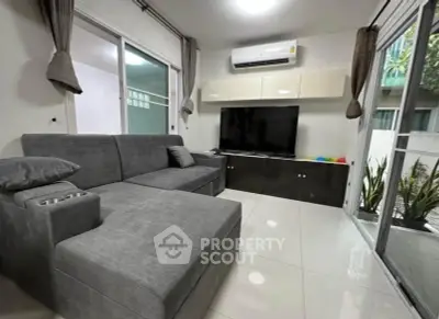 Modern living room with sleek gray sectional sofa and large TV, featuring floor-to-ceiling windows and stylish decor.