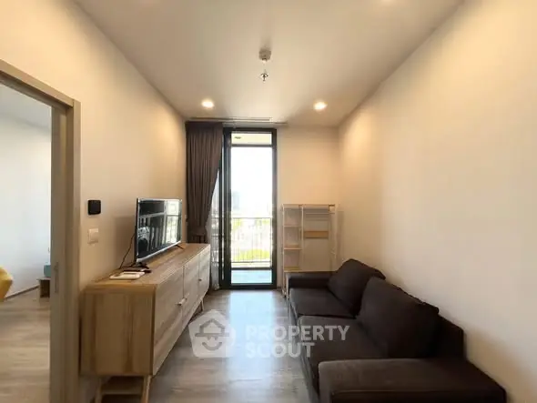 Modern living room with sleek furniture and large window leading to a balcony, offering a bright and airy space.