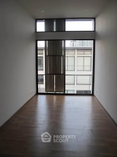 Spacious empty room with large window and wooden flooring, ideal for customization.
