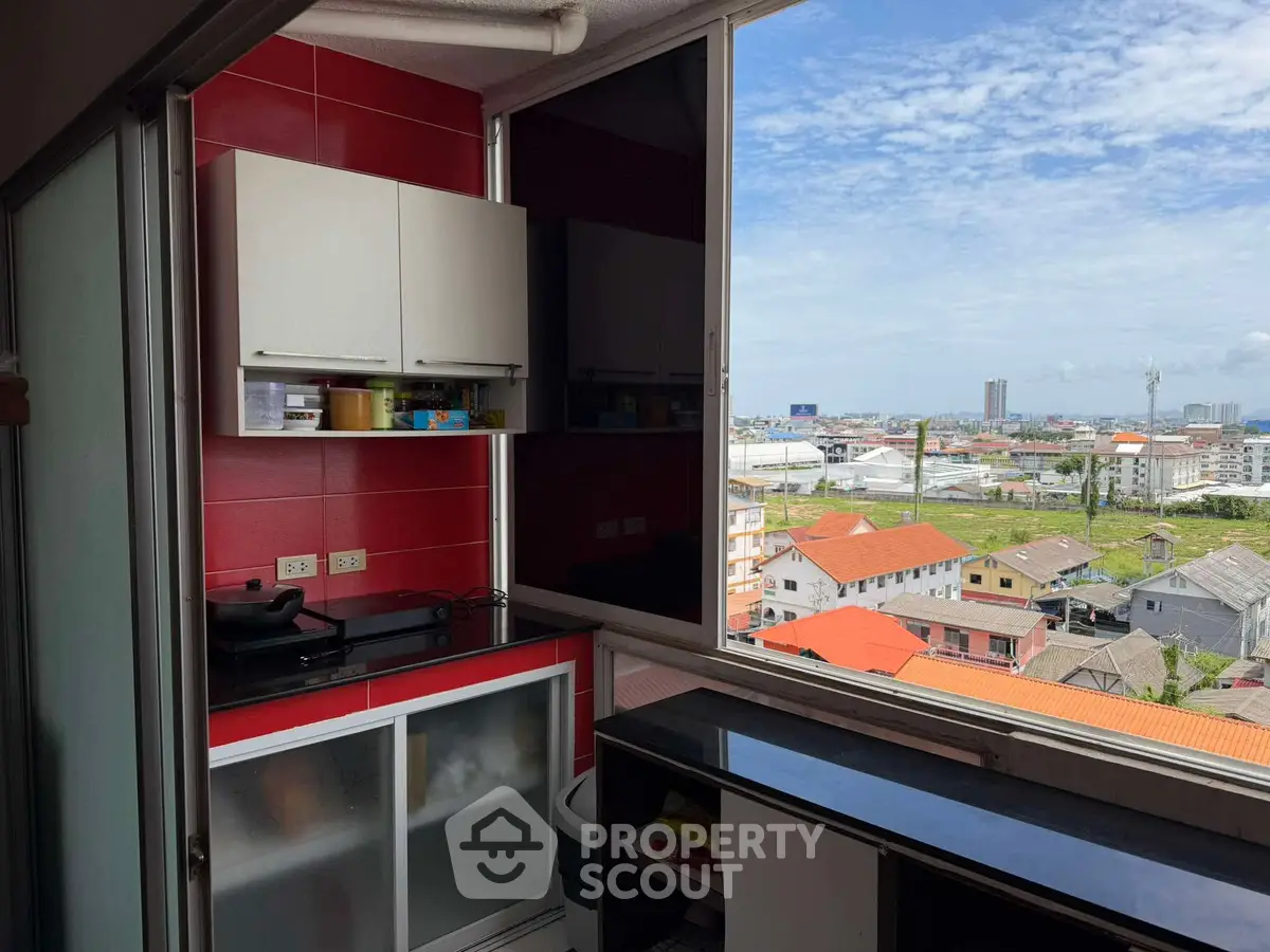 Compact kitchen with vibrant red backsplash and stunning city view from high-rise apartment.