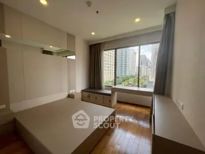 Modern bedroom with large window offering stunning city view and sleek built-in furniture.