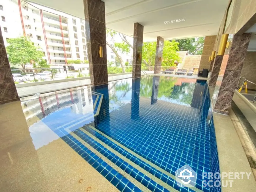 Luxurious residential complex pool with reflective water surface, surrounded by elegant columns and a view of the urban landscape.