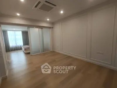 Spacious empty room with wooden flooring and sliding doors leading to a bedroom with natural light.