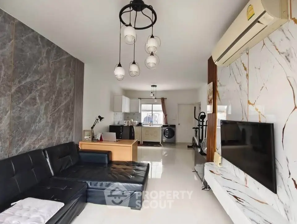 Modern living room with sleek black sofa, marble accents, and open kitchen layout.