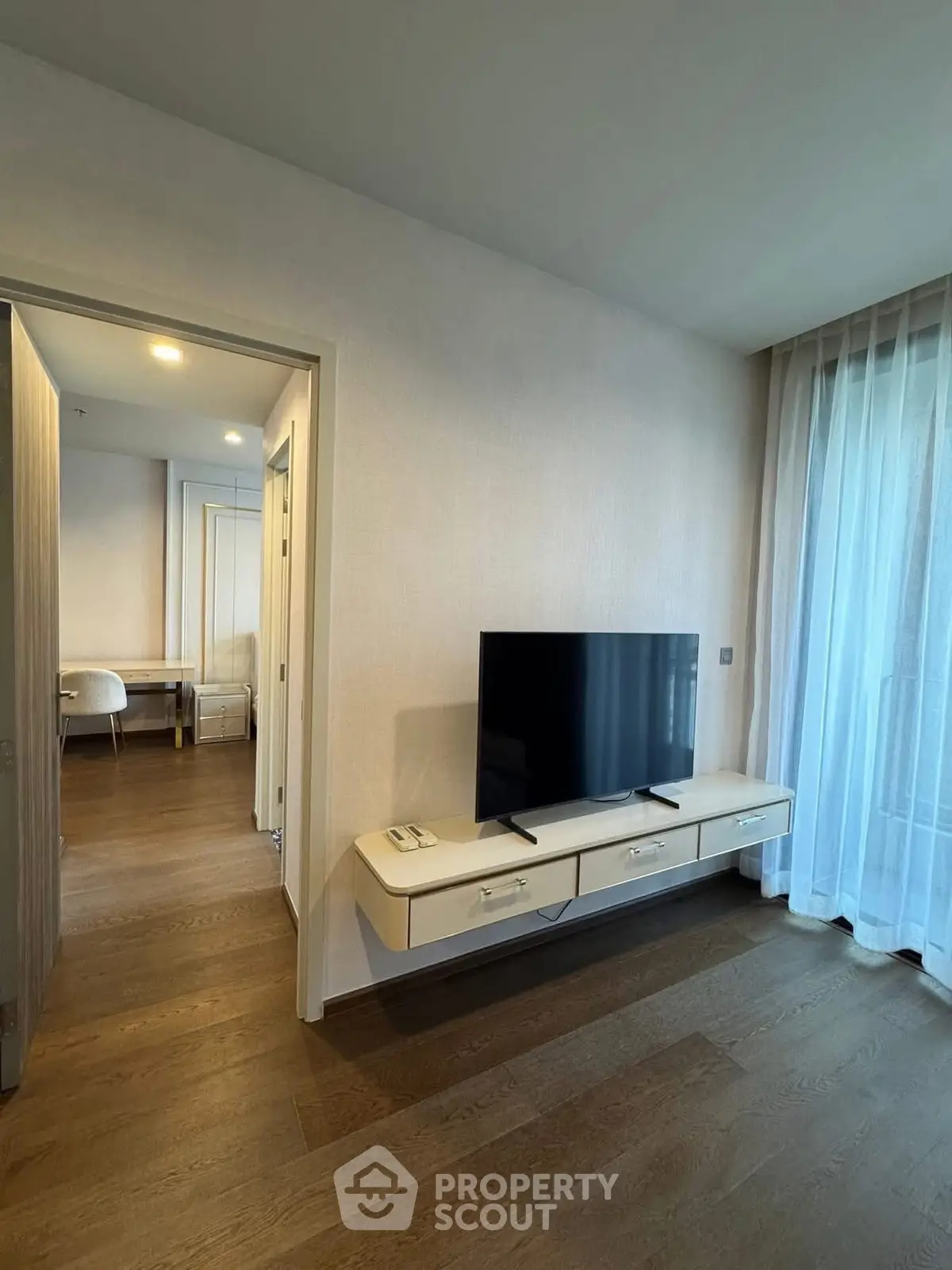 Modern living room with sleek TV stand and large window with sheer curtains, showcasing elegant interior design.