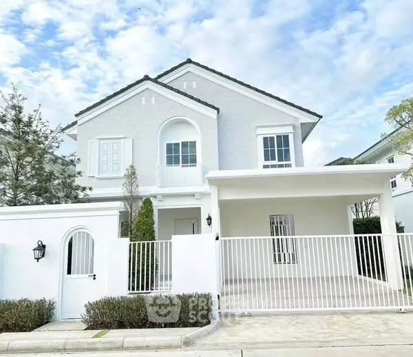Charming white two-story house with gated driveway and lush greenery.
