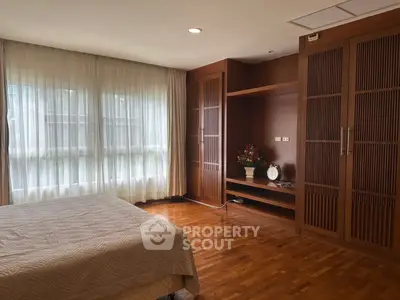 Spacious bedroom with elegant wooden flooring and large windows for natural light.