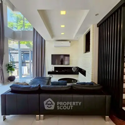 Modern living room with high ceilings, sleek black sofa, and large windows offering natural light.