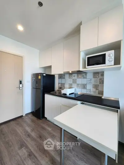 Modern kitchen with sleek cabinets, black fridge, and microwave in stylish apartment.