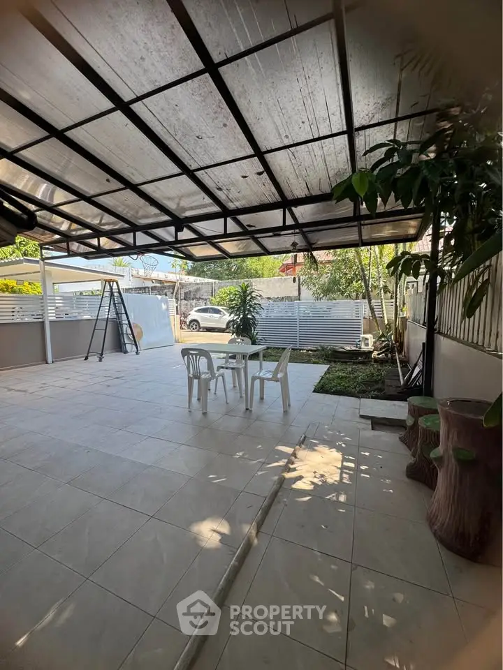 Spacious covered patio with outdoor seating and garden view, perfect for relaxation and entertaining.