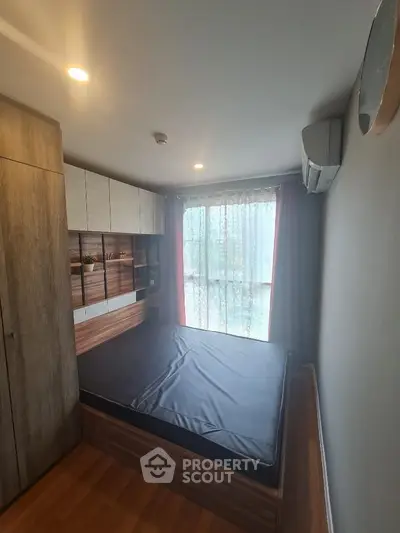 Cozy bedroom with modern wooden furnishings and large window for natural light.