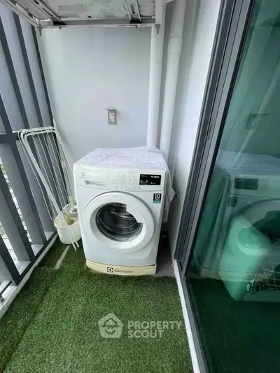 Compact balcony with washing machine and artificial grass flooring in modern apartment.