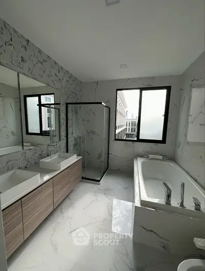 Luxurious modern bathroom with dual sinks, large bathtub, and glass shower enclosure.