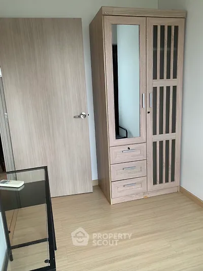 Modern bedroom with sleek wardrobe and glass desk, featuring minimalist design and light wood flooring.