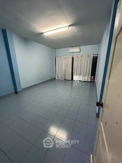 Spacious empty room with tiled flooring and large window, ideal for customization.
