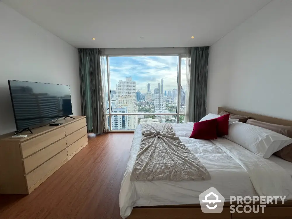 Spacious bedroom with city view, modern furniture, and large window for natural light.