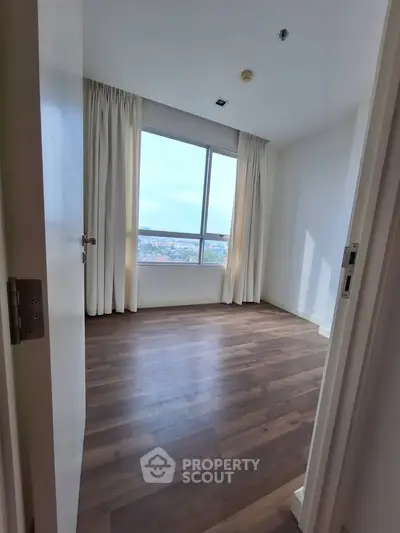 Spacious bedroom with large window offering stunning city views and elegant wooden flooring.