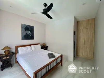 Spacious bedroom with polished tile flooring, modern ceiling fan, and wooden wardrobe, complemented by minimalist decor and artwork.