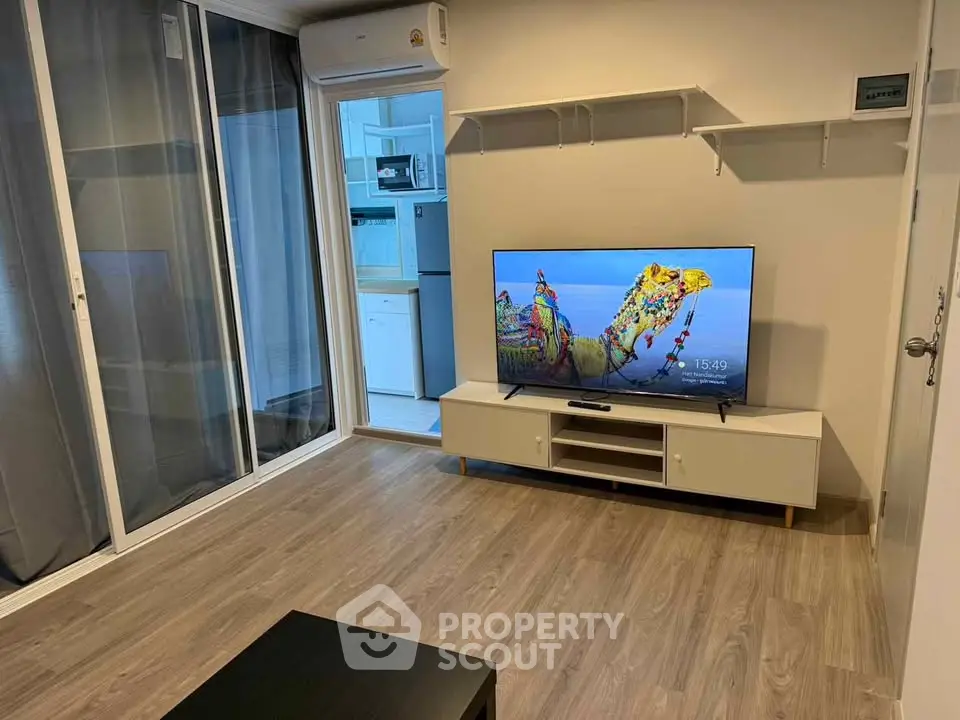 Modern living room with sleek flooring and wall-mounted TV, adjacent to a compact kitchen area.