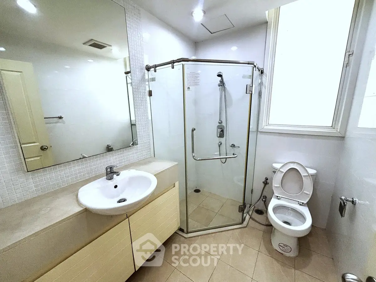 Modern bathroom with glass shower, sleek sink, and toilet in bright, clean setting.