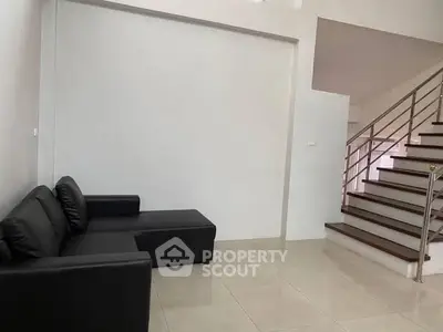 Modern minimalist living room with sleek black sofa and staircase