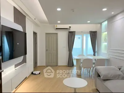 Modern living room with sleek furniture and natural light, featuring a wall-mounted TV and dining area.