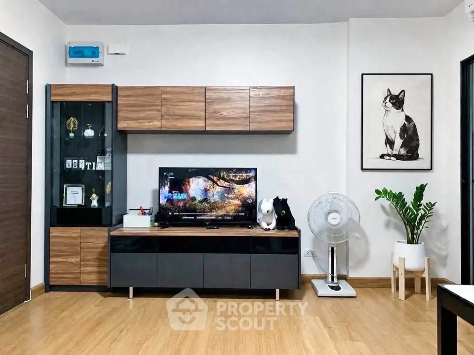 Modern living room with stylish wooden cabinets and TV setup, featuring a cat artwork and indoor plant.