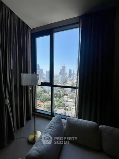 Modern living room with floor-to-ceiling windows offering stunning city views, featuring a cozy sofa and elegant lamp.