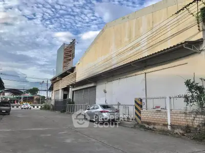 Spacious industrial warehouse exterior with ample parking space and secure fencing.