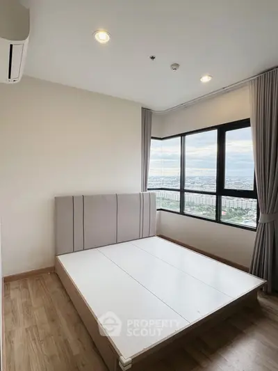 Spacious bedroom with large windows offering stunning city views, featuring a modern bed frame and elegant curtains.