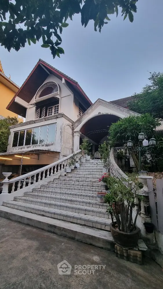 Charming colonial-style house with grand staircase and lush greenery