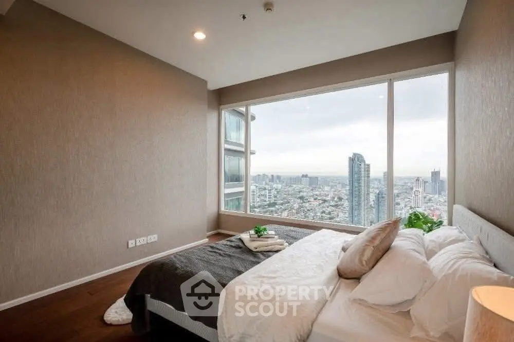 Luxurious bedroom with stunning city view from large window in high-rise apartment.