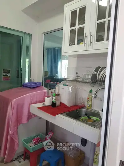 Compact kitchen with white cabinets and sink, featuring a small dining area.