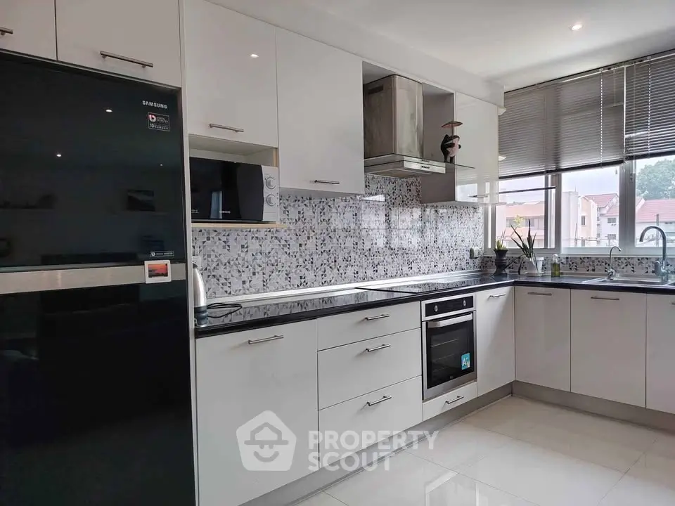 Modern kitchen with sleek white cabinets, mosaic backsplash, and stainless steel appliances.