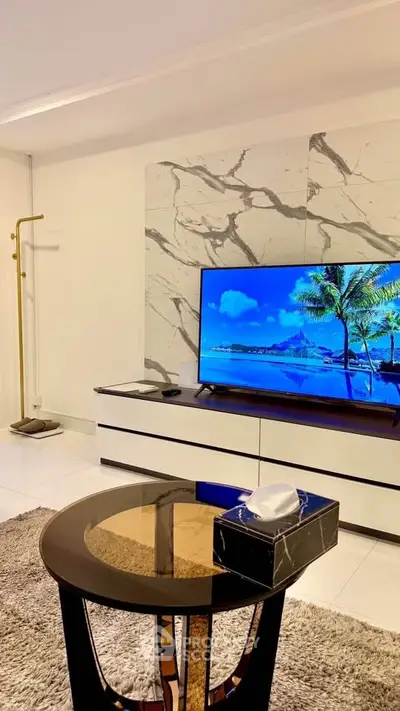 Modern living room with stylish decor and large flat-screen TV, featuring marble accent wall and elegant furniture.