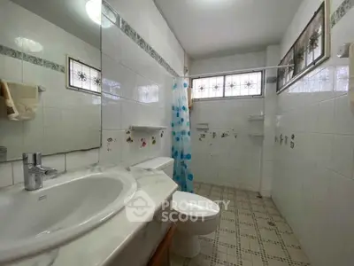 Spacious bathroom with tiled walls and modern fixtures, featuring a large mirror and natural light.