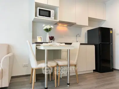 Modern kitchen with sleek cabinets, dining table, and appliances in a cozy apartment setting.