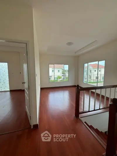 Spacious interior with wooden flooring and large windows offering natural light and neighborhood view.