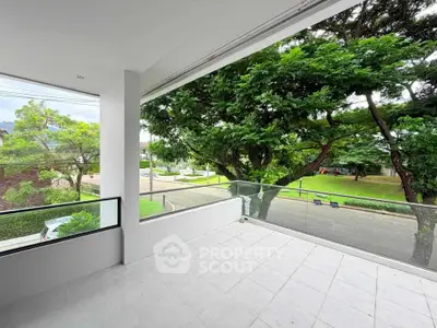 Spacious balcony with glass railing and lush green view in modern residential area.