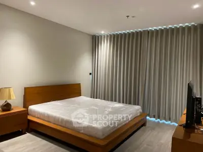 Spacious modern bedroom with wooden furniture and large window curtains.