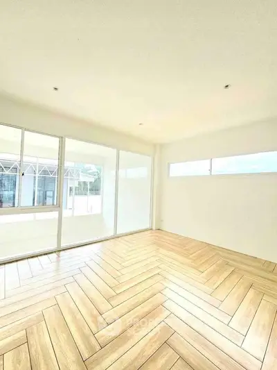 Spacious sunlit room with large windows and elegant herringbone wooden flooring.