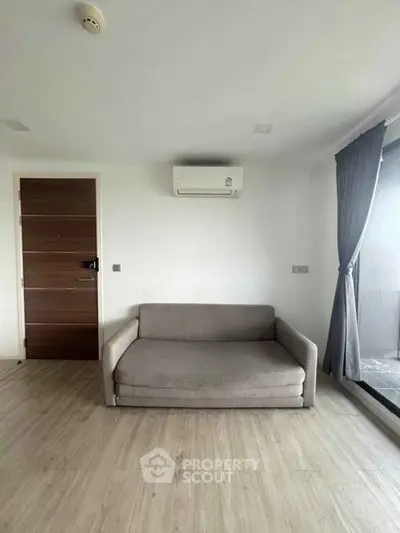 Modern living room with sleek sofa and air conditioning, featuring large window for natural light.