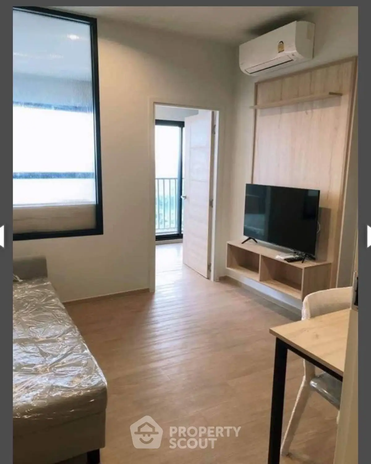 Modern living room with wooden flooring, TV setup, and air conditioning in a cozy apartment.