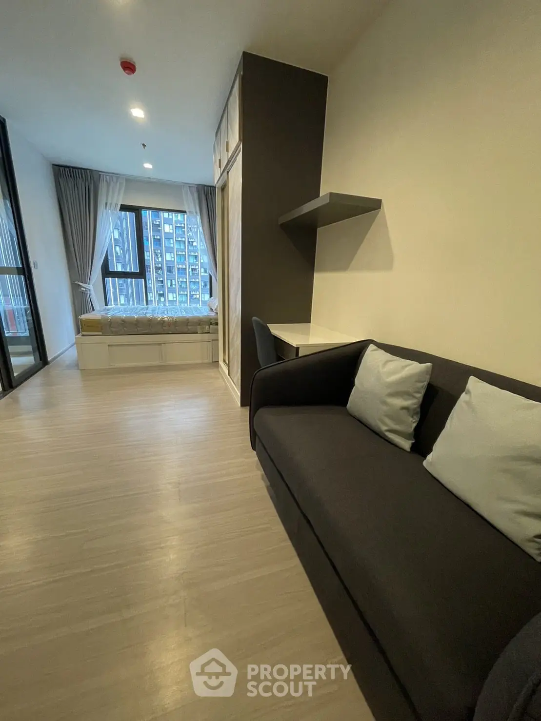 Modern living room with sleek dark sofa, floating shelves, and expansive windows offering a city view, in a chic urban apartment.