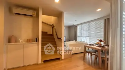 Modern living room with dining area and staircase, featuring wooden flooring and natural light.