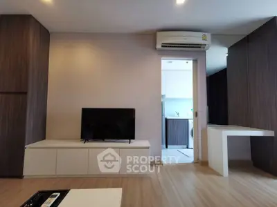 Modern living room with sleek design and open view to kitchen area, featuring wooden flooring and air conditioning.