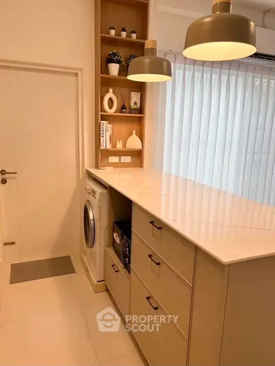 Modern kitchen with sleek cabinetry and built-in washing machine, featuring elegant lighting and minimalist decor.