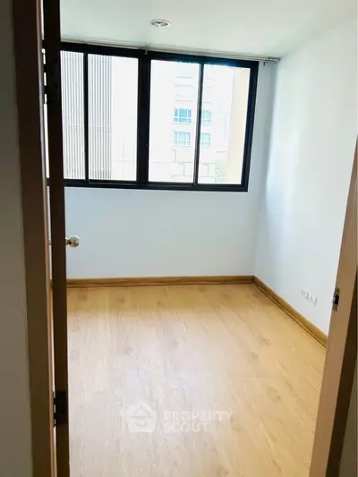 Bright empty room with wooden flooring and large window in modern apartment.
